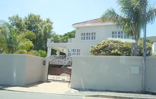 Two-storey house behind a boundary wall with a wrought-iron pedestrian gate